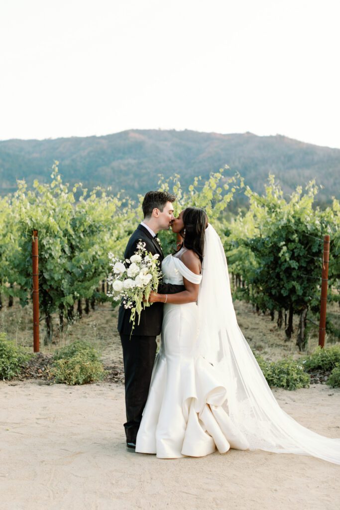 Bride and groom kissing among Napa Valley vineyard rows at their Tre Posti wedding in Saint Helena