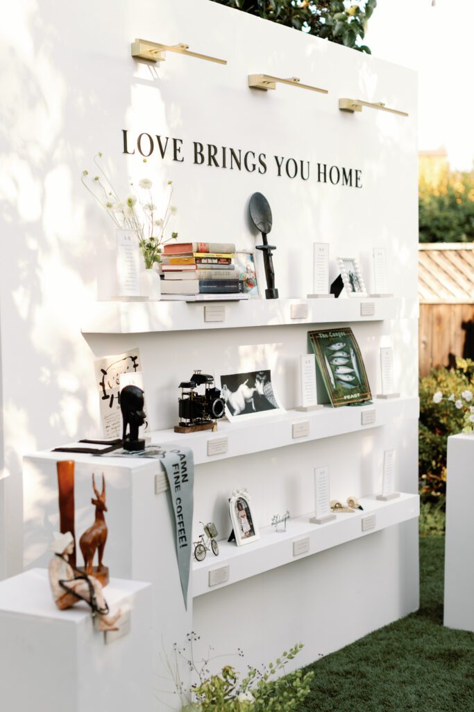 Personalized wedding escort card wall with books, photographs, and keepsakes reading Love Brings You Home