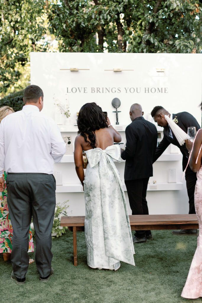Personalized wedding escort card wall with books, photographs, and keepsakes reading Love Brings You Home